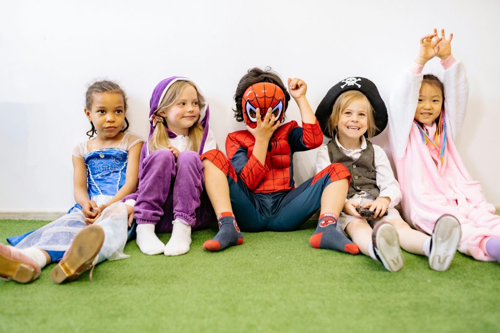 A group of children in various costumes enjoying playtime indoors on a green carpet.